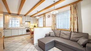 A modern kitchen with white cabinets, a dining area with a table and chairs, and a grey sectional sofa in a living area with large windows and curtains. - Pet-Friendly Holiday Apartment 'Kuenz Dolomiten Drau' with Mountain View (San Candido)