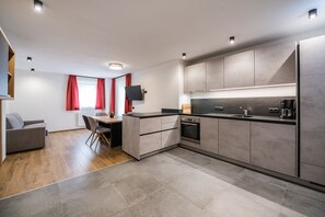 Una cocina moderna con armarios grises, horno empotrado y zona de comedor con mesa y sillas.