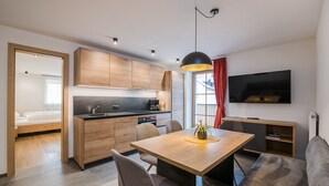 Eine moderne Küche mit Holzausstattung, einem Esstisch und Stühlen. Ein Fernseher ist an der Wand befestigt und im Wohnbereich steht eine Couch.