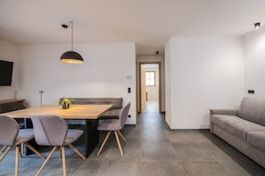 Een moderne woonkamer met een bank, een eettafel met stoelen, een hanglamp en uitzicht op een andere kamer.