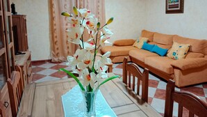 A living room with a sofa, a dining table with a vase of flowers, a television, and a wall-mounted air conditioner. - Holiday Home La Reconquista with Pool, Garden & Wi-Fi (Santa Elena)