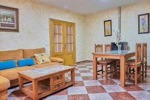 Un salon comprenant un canapé, une table basse en bois, une table à manger avec des chaises, une porte et des œuvres d’art accrochées au mur.