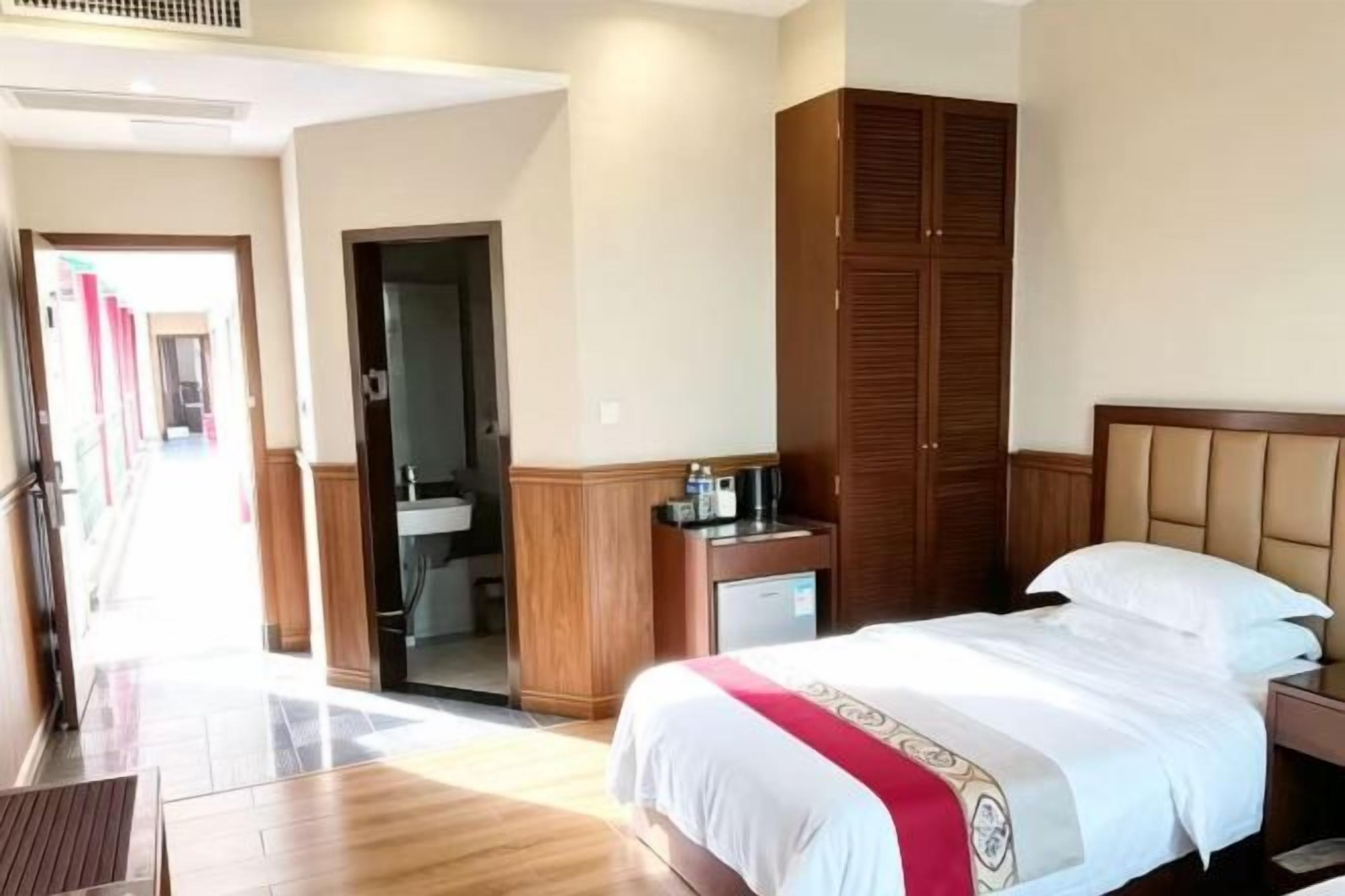 A hotel room with a bed, a wardrobe, a bedside table, and a bathroom visible through an open door.