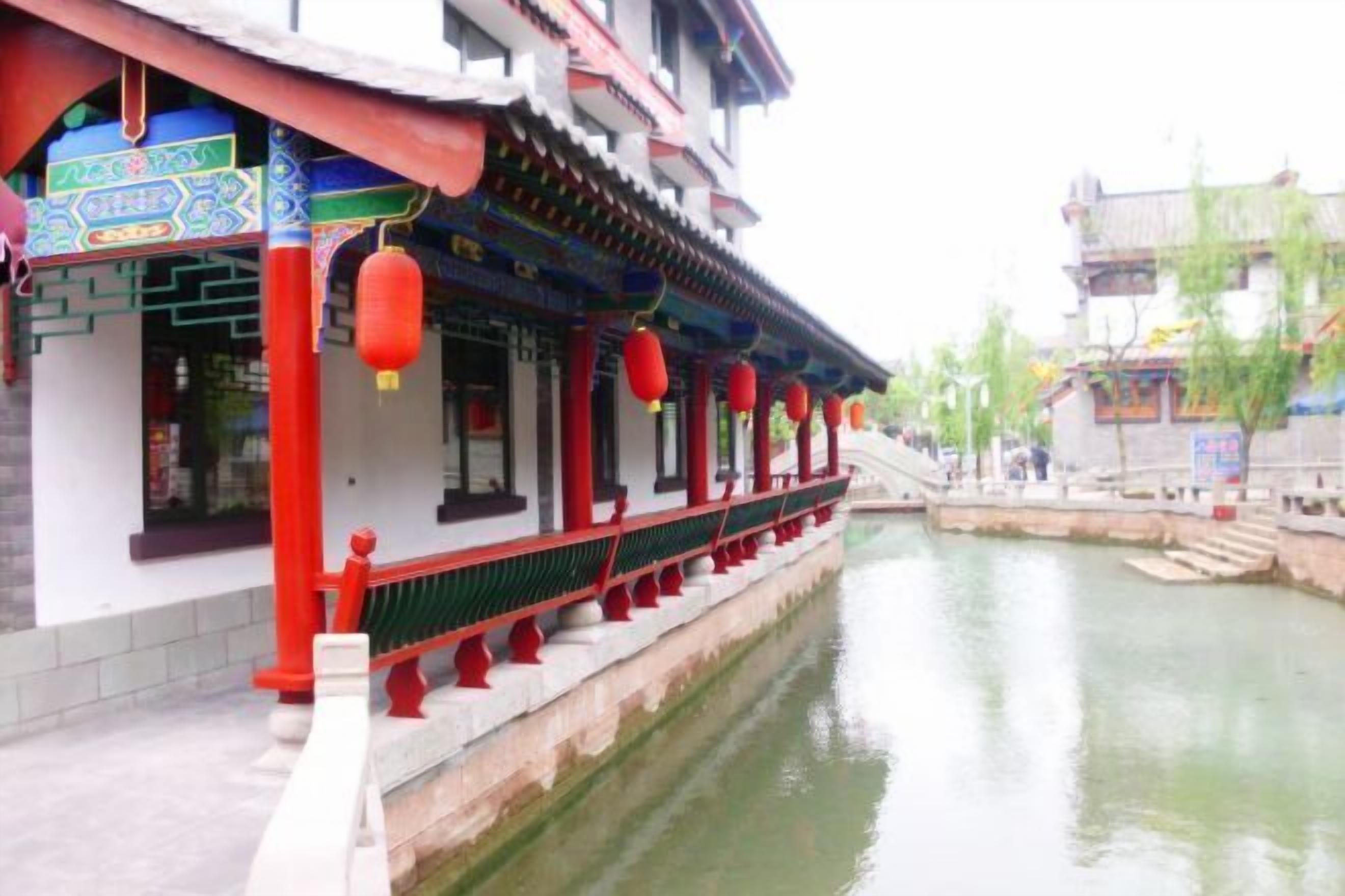 A traditional building with a waterway in front, featuring a red and white facade, and a bridge leading to the building.