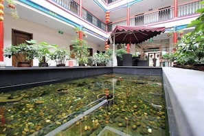 Un atrio de varios niveles con una fuente central, plantas en macetas y una zona de estar cubierta.