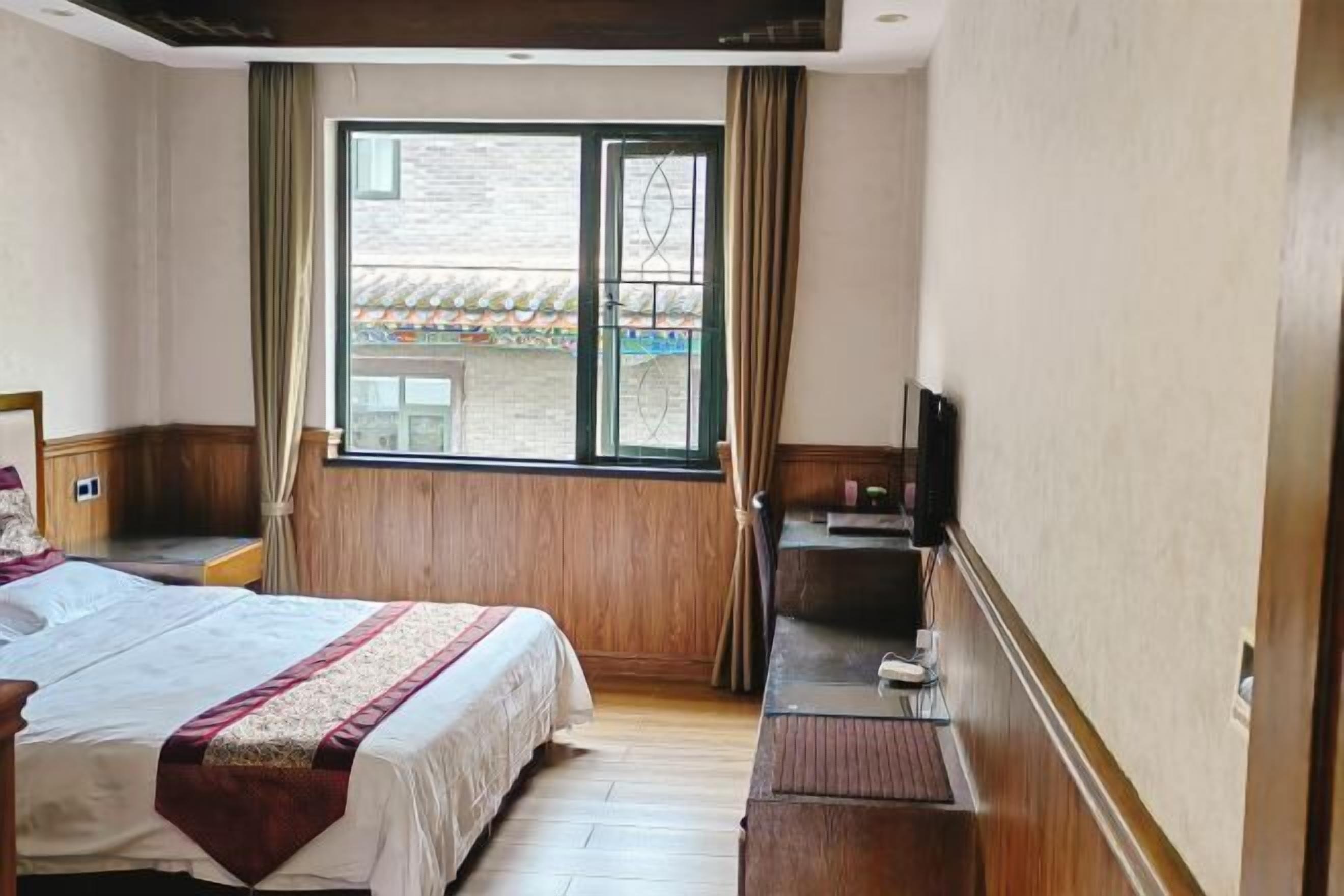 Una habitación de hotel con cama, escritorio con televisor y ventana con cortinas.