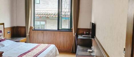 Una habitación de hotel con cama, escritorio con televisor y ventana con cortinas.