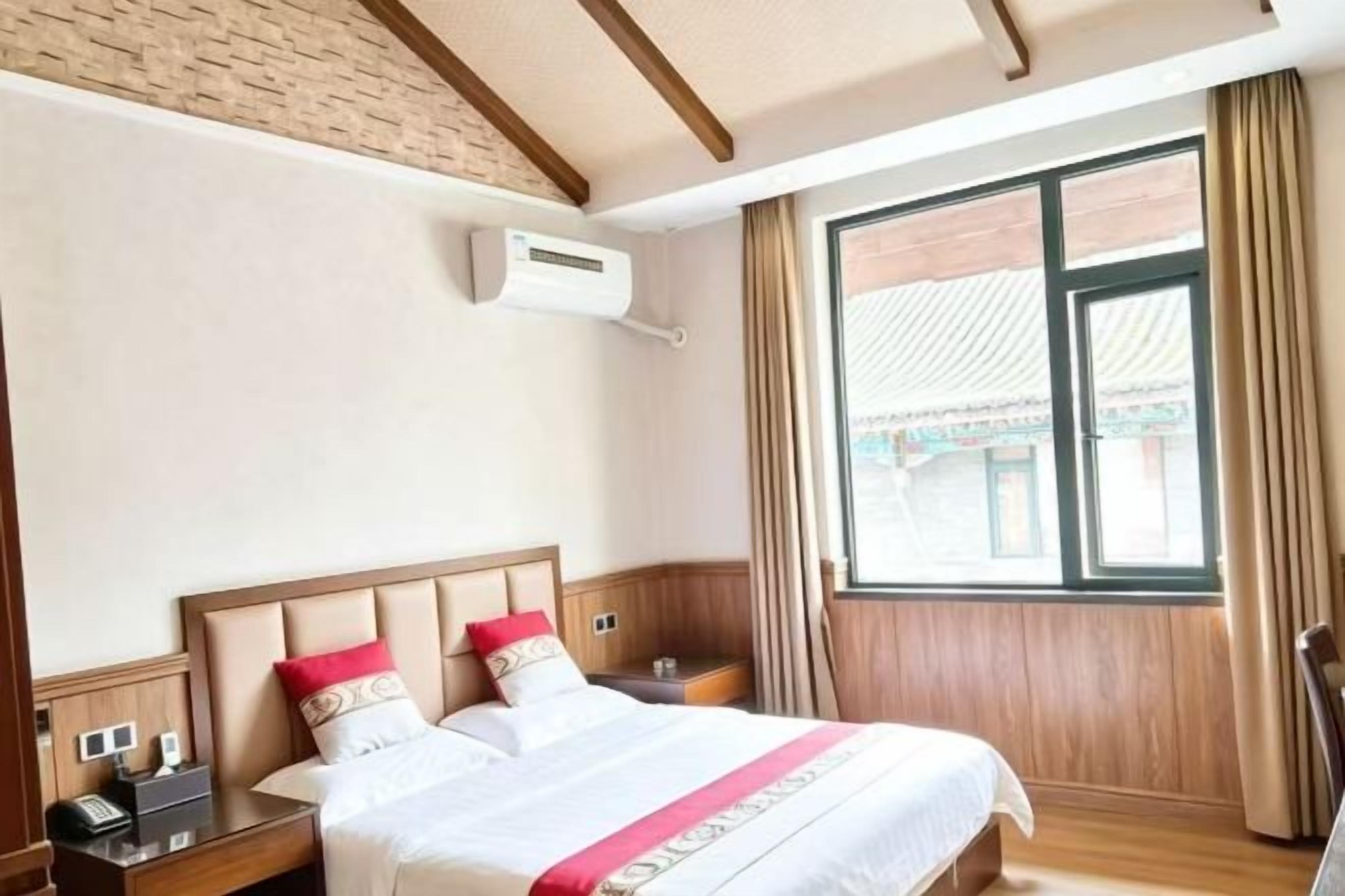 Et hotelværelse med en stor seng, sengeborde, en aircondition og et vindue med gardiner.
