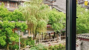 A traditional courtyard with a wooden bridge, surrounded by lush greenery and traditional architecture. - Qincaige Hostel (Chongqing)