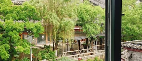 A traditional courtyard with a wooden bridge, surrounded by lush greenery and traditional architecture.