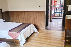 Quarto de hotel com piso de madeira, cama com roupa de cama branca e manta vermelha e bege, e guarda-roupa de madeira.