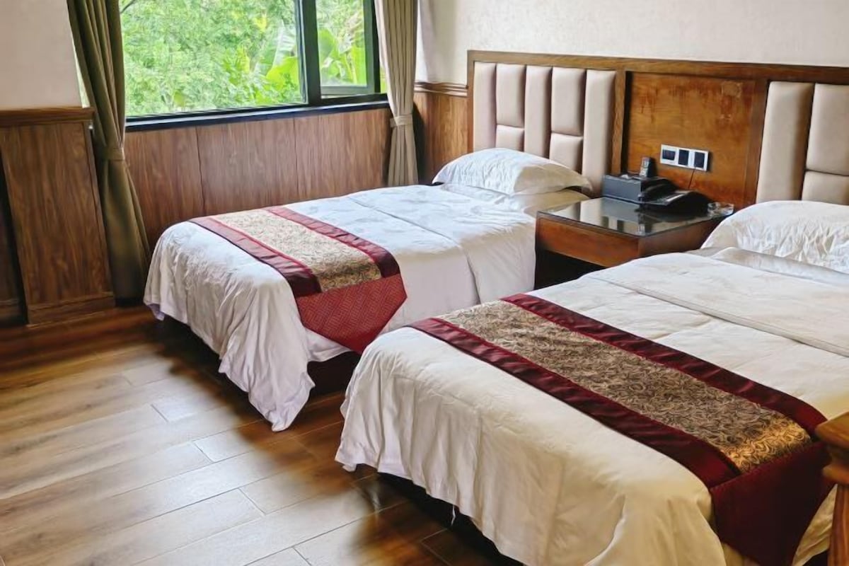 Habitación de hotel con dos camas, suelo de madera, cabecero de madera y una ventana con cortinas.