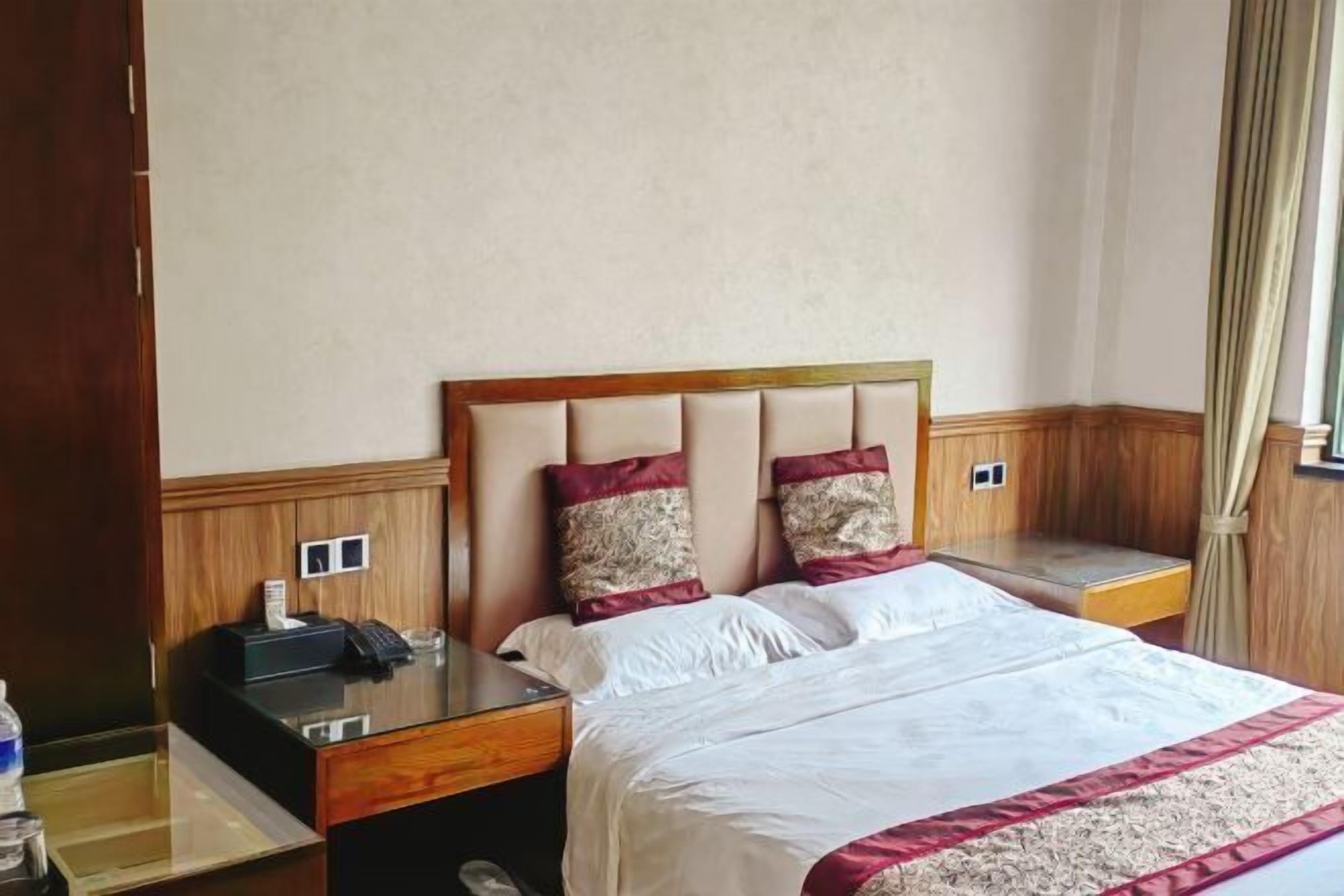 Une chambre d’hôtel comprenant un lit, une table de chevet avec un téléphone et une lampe, un petit coin salon et une fenêtre avec des rideaux.