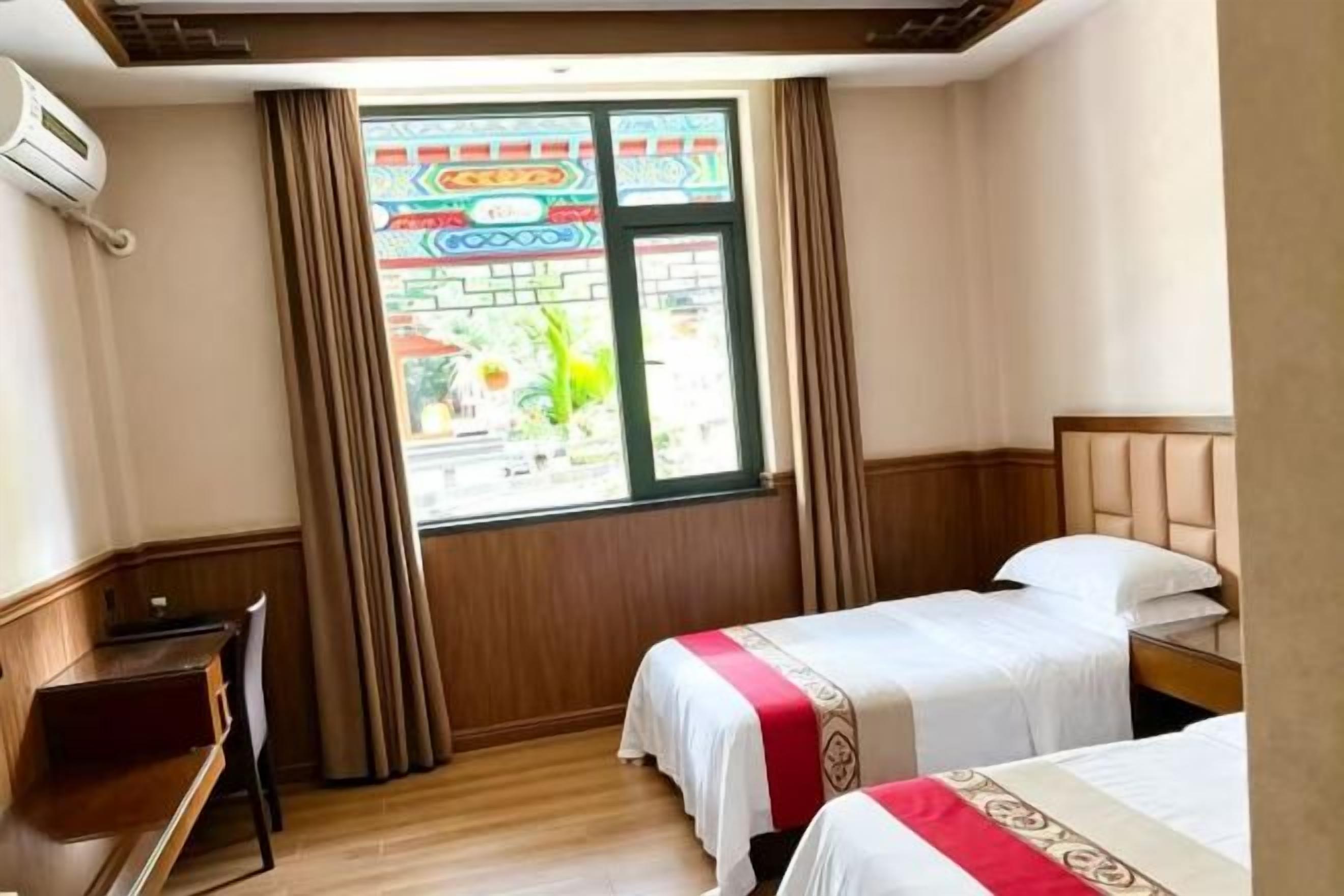 A hotel room with two beds, a desk, and a window with curtains.