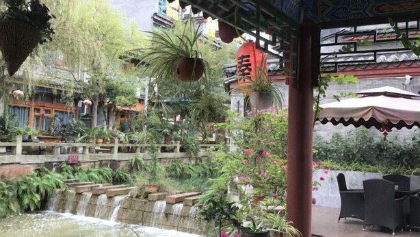 A traditional courtyard with a small waterfall, potted plants, and outdoor seating. - Qincaige Hostel (Chongqing)
