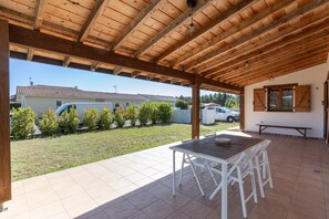 Een terras buiten met een houten pergola, een tafel en stoelen, en uitzicht op een woonwijk.