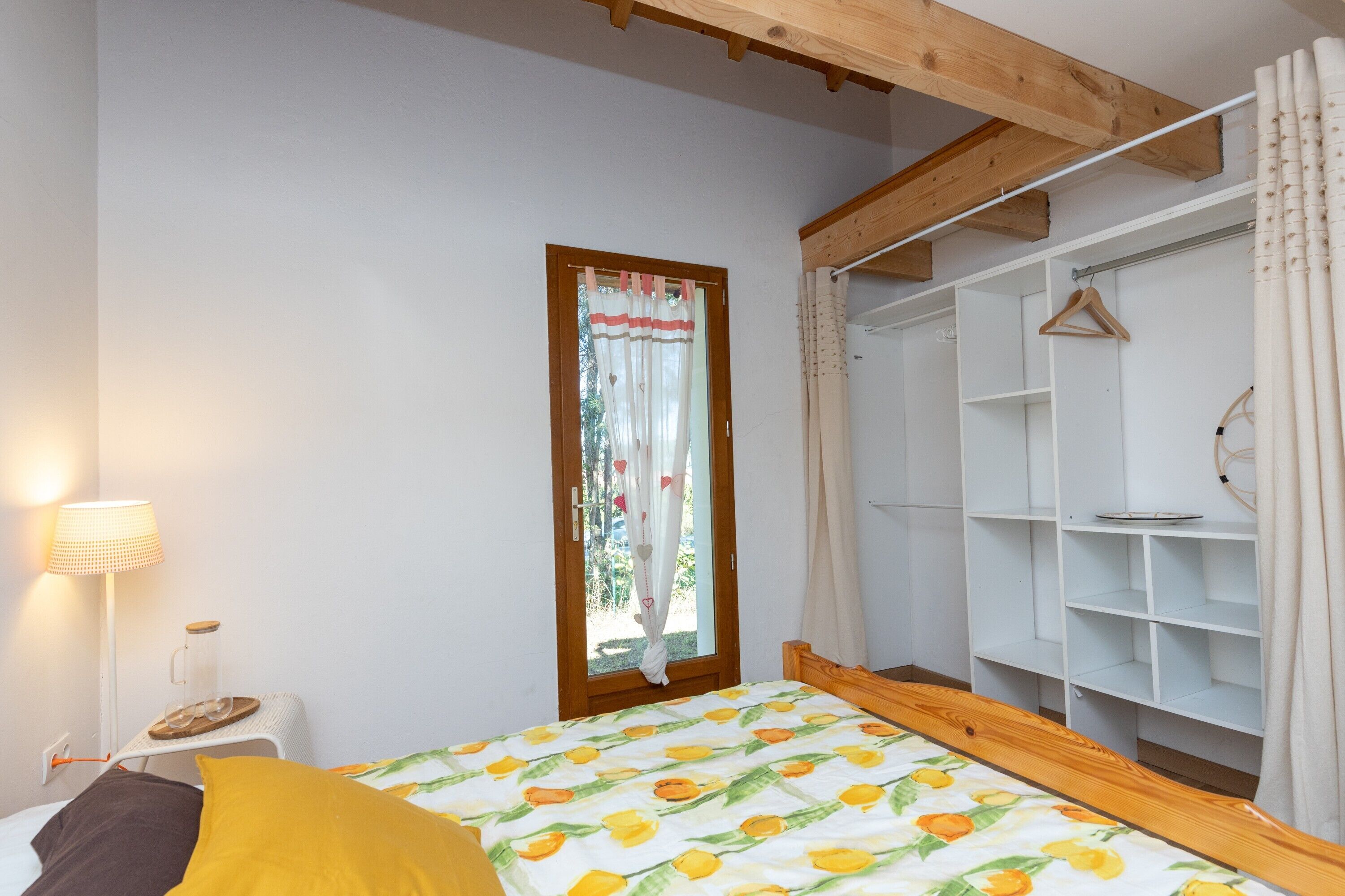 A bedroom with a bed, a bedside table with a lamp, a wardrobe, and a window with curtains.