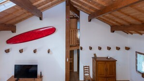 Una habitación con televisor sobre un mueble de madera, una tabla de surf roja en la pared y techo de madera.