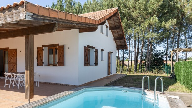 Un edificio blanco con piscina, contraventanas de madera y una pérgola.