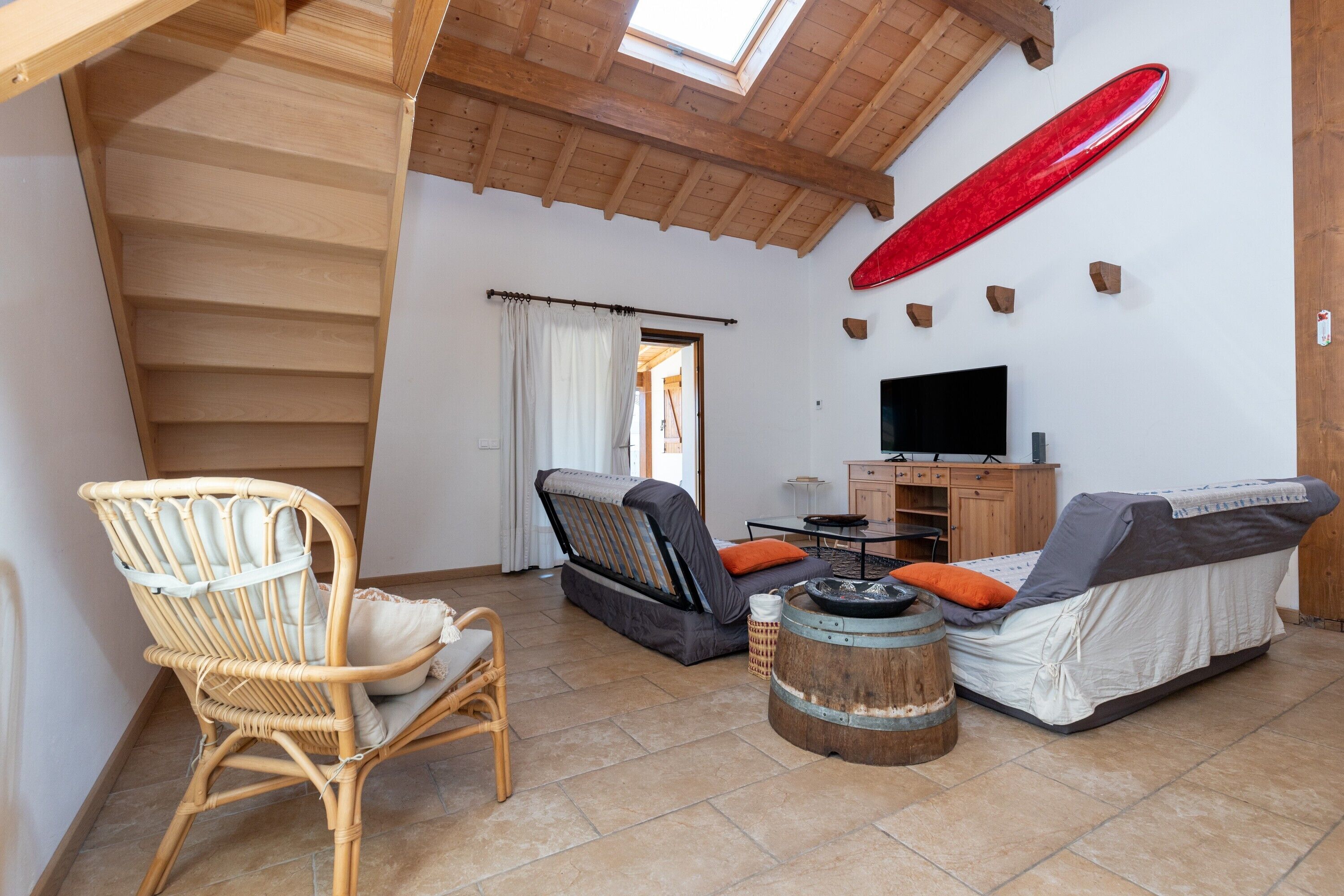 Ein Zimmer mit Holzboden, einem Fernseher, einem Sofa, einem Sessel und einem Surfbrett an der Wand.