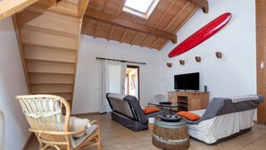 Una habitación con techo de madera, televisor, sofá, silla y una tabla de surf en la pared.