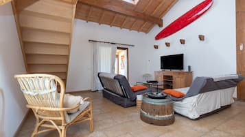 Ein Zimmer mit Holzboden, einem Fernseher, einem Sofa, einem Sessel und einem Surfbrett an der Wand.