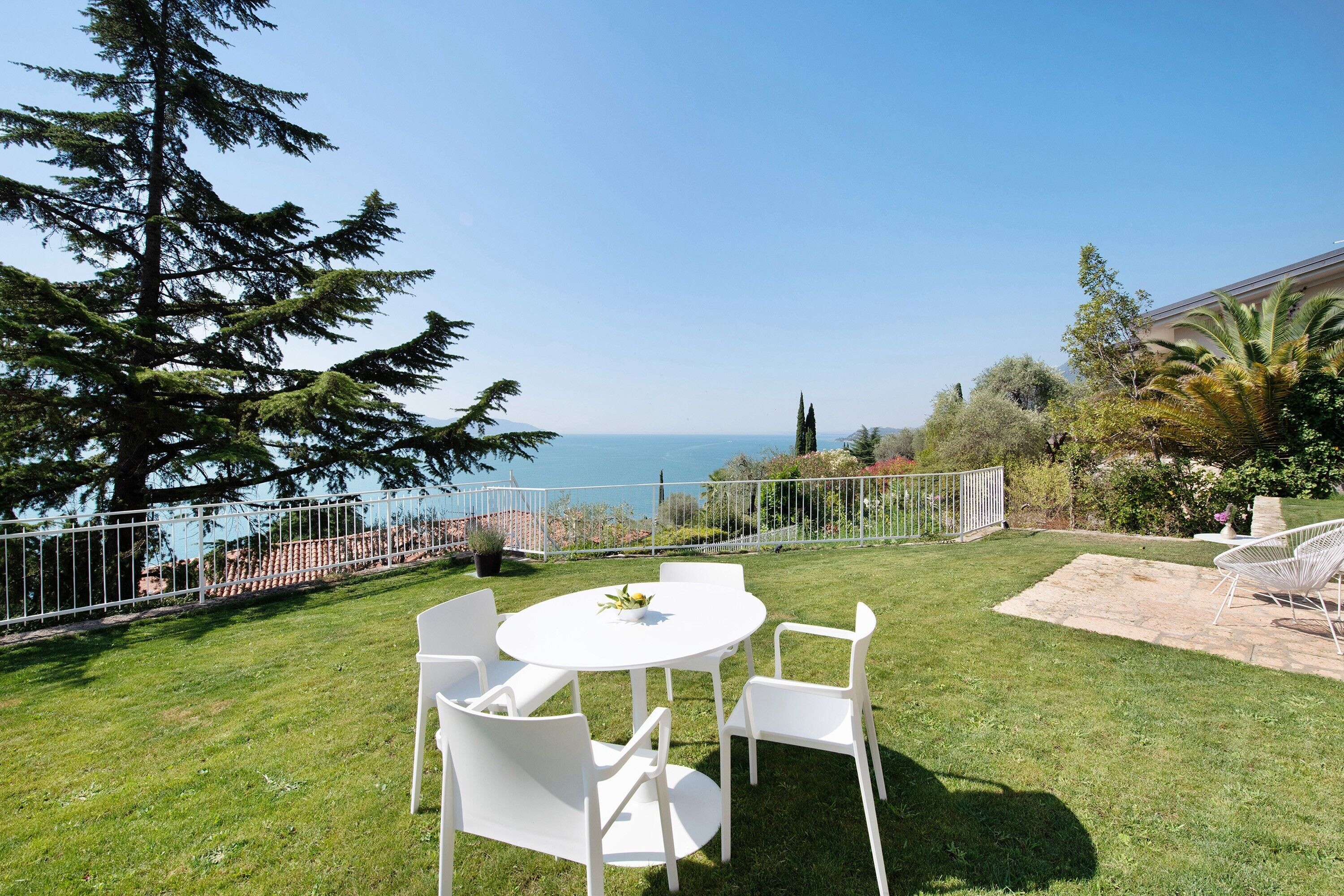 Une terrasse avec une table et des chaises blanches, un sol en pierre et une vue sur la mer.