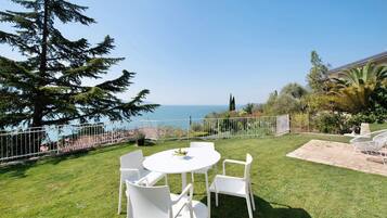 Une terrasse avec une table et des chaises blanches, un sol en pierre et une vue sur la mer.
