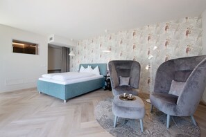A modern bedroom with a bed, two armchairs, a small table, and a patterned wall.