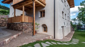 Un edificio moderno con fondamenta in pietra, un balcone in legno e un viale in pietra che conduce all'ingresso.