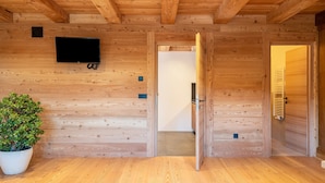 Un interno in legno con una TV montata a parete, una pianta in vaso e una porta che dà su un'altra stanza.