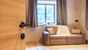 Una porta in legno con maniglia e serratura nera, che dà su una stanza con un divano beige e una finestra con tende.