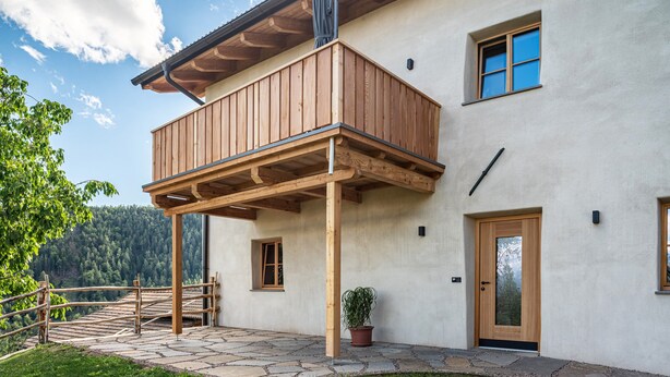 A two-story building with a wooden balcony, stone flooring, and a view of a forested area. - Holiday Apartment Egger an der Lahn - Nonno with Mountain View, Terrace and Wi-Fi (San Genesio)