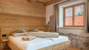 Quarto com painéis de madeira, uma cama, parede de pedra e janela com cortinas.