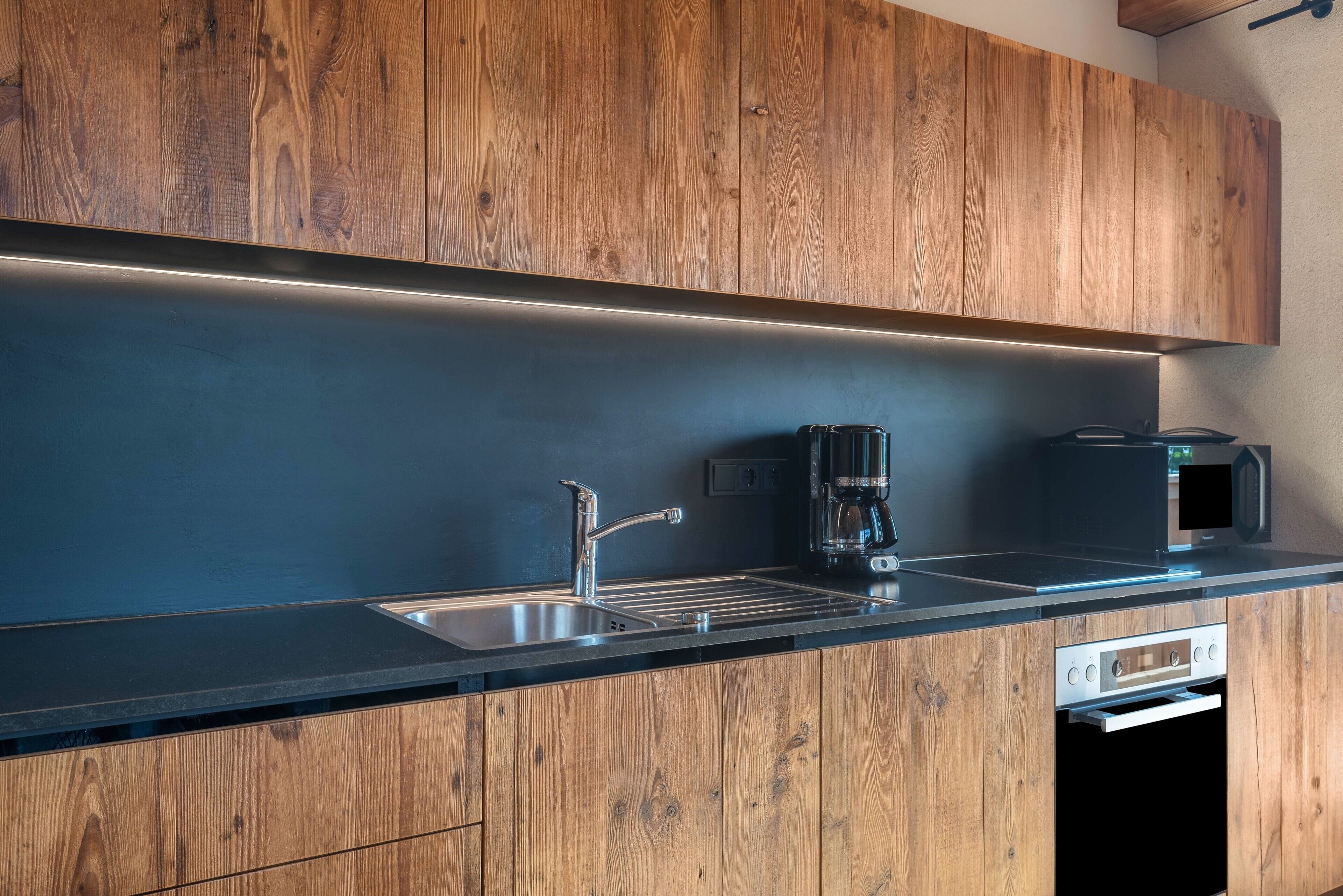 Una cocina moderna con armarios de madera, un lavamanos de acero inoxidable y un horno empotrado.