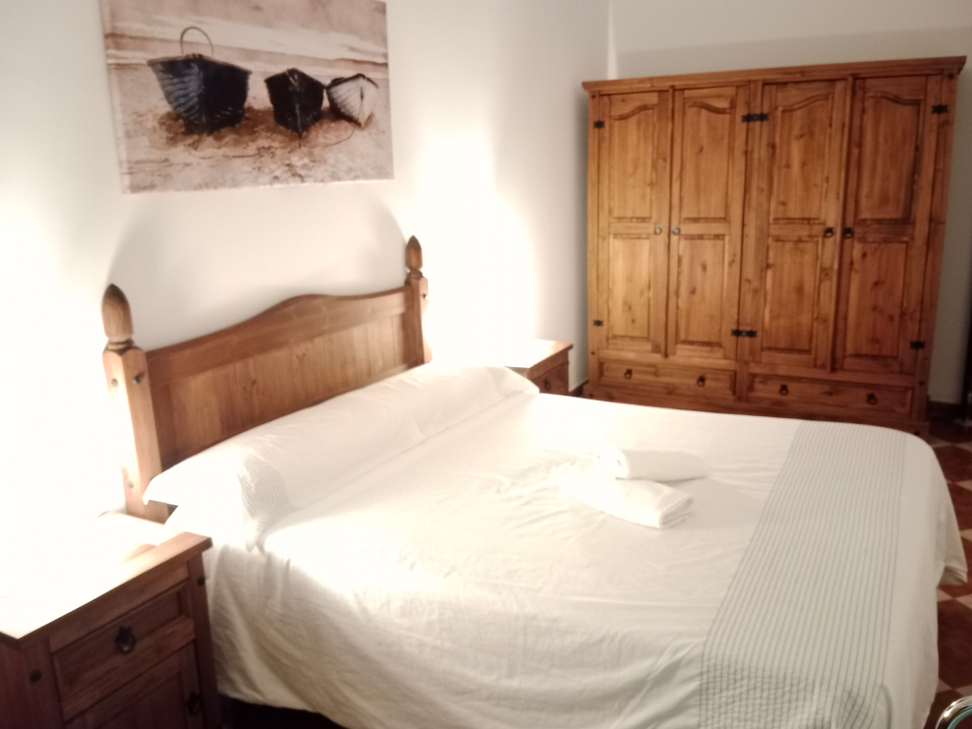 A bedroom with a wooden bed, a wooden wardrobe, and a wall-mounted picture.