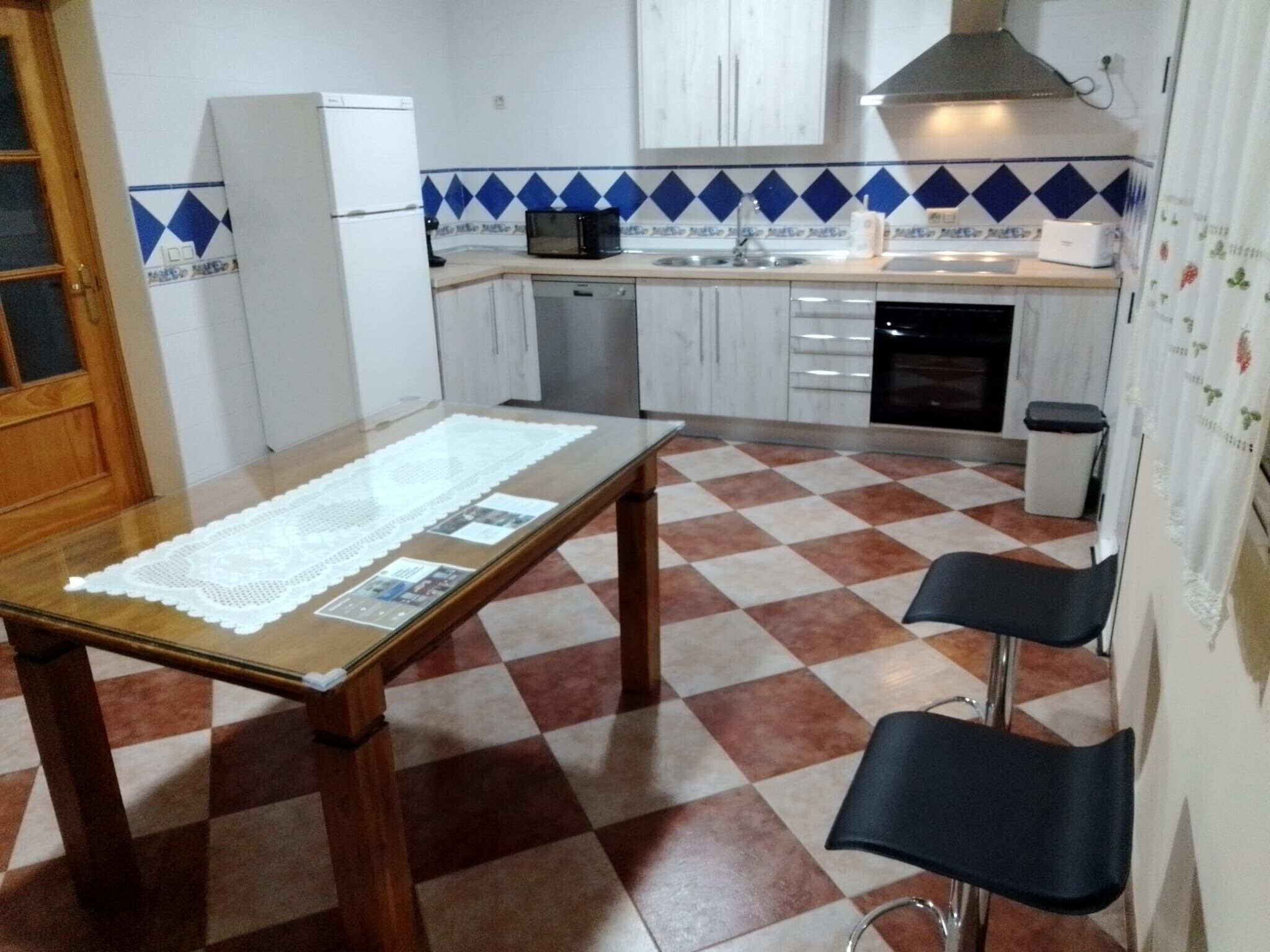 A kitchen with a checkered floor, a table with a lace tablecloth, and a microwave.