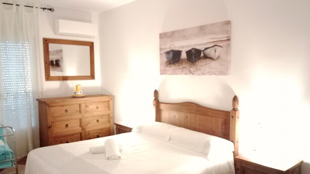 Un dormitorio con una cama de madera, un tocador de madera, un espejo y un cuadro en la pared.