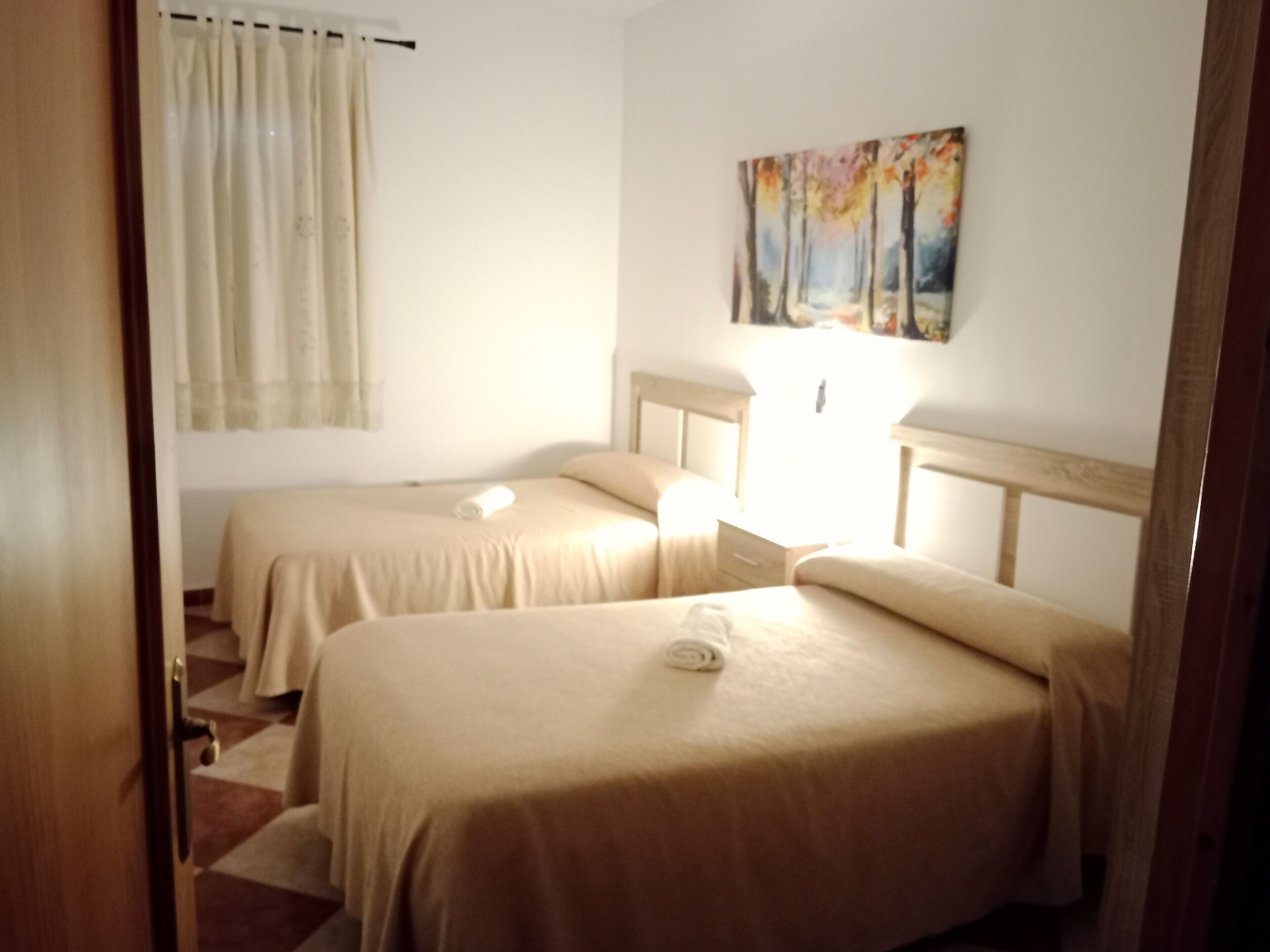 Habitación de hotel con dos camas, un cuadro en la pared y una ventana con cortinas.