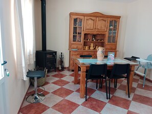 Un comedor con piso a cuadros, un mueble de madera con puertas de vidrio, una mesa con sillas y una estufa negra.