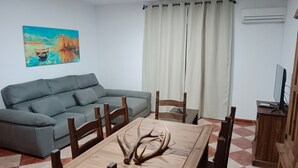 Una sala de estar con un sofá gris, una mesa de comedor de madera con cuernos de ciervo y un televisor sobre un mueble de madera.