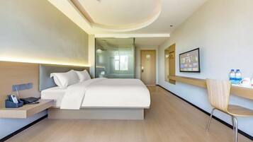 A modern hotel room with a bed, bedside table, chair, and a view of the hallway.