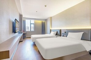 Ett hotellrum med två sängar, ett skrivbord, en stol, en TV och utsikt över staden.