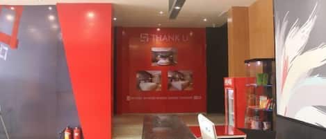 A reception area with a red wall, a 'THANK U' sign, and a counter with a computer and a beverage dispenser.