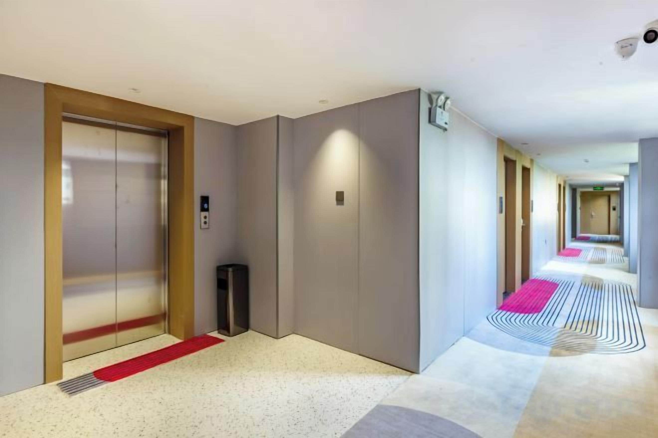 A hotel corridor with a red carpet, a trash bin, and a security camera.