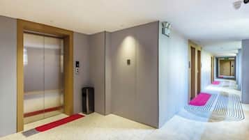 A hotel corridor with a red carpet, a trash bin, and a security camera.