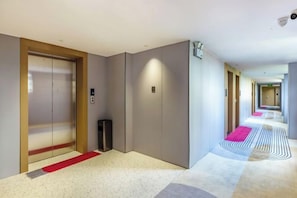 Corredor de hotel com carpete vermelho, uma lixeira e uma câmera de segurança.