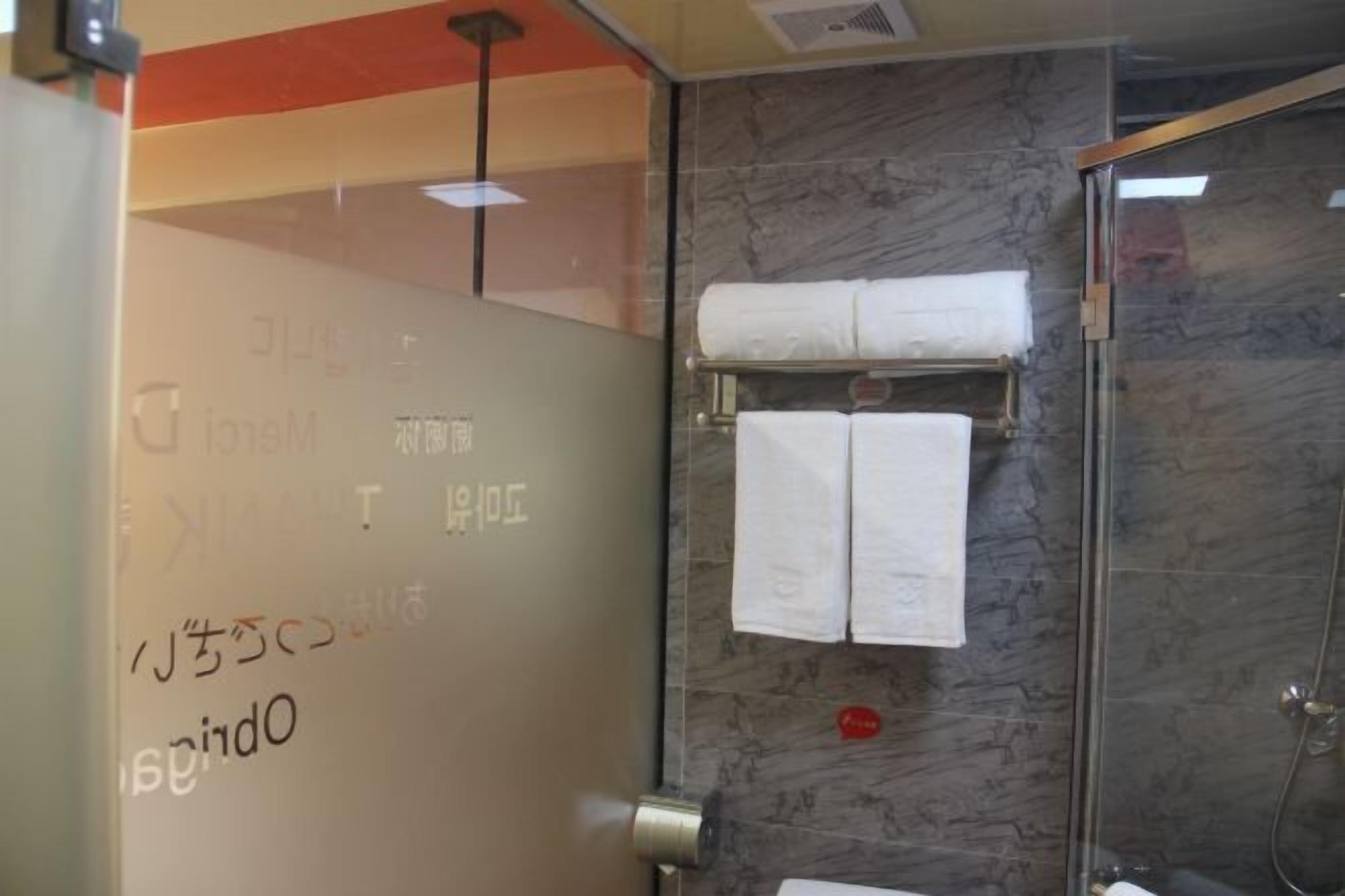 A bathroom with a glass shower enclosure, marble walls, and a towel rack with two towels.