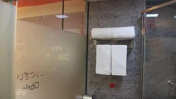 A bathroom with a glass shower enclosure, marble walls, and a towel rack with two towels.