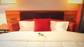 A hotel room with a large bed, a wooden headboard, two bedside lamps, and a red pillow.